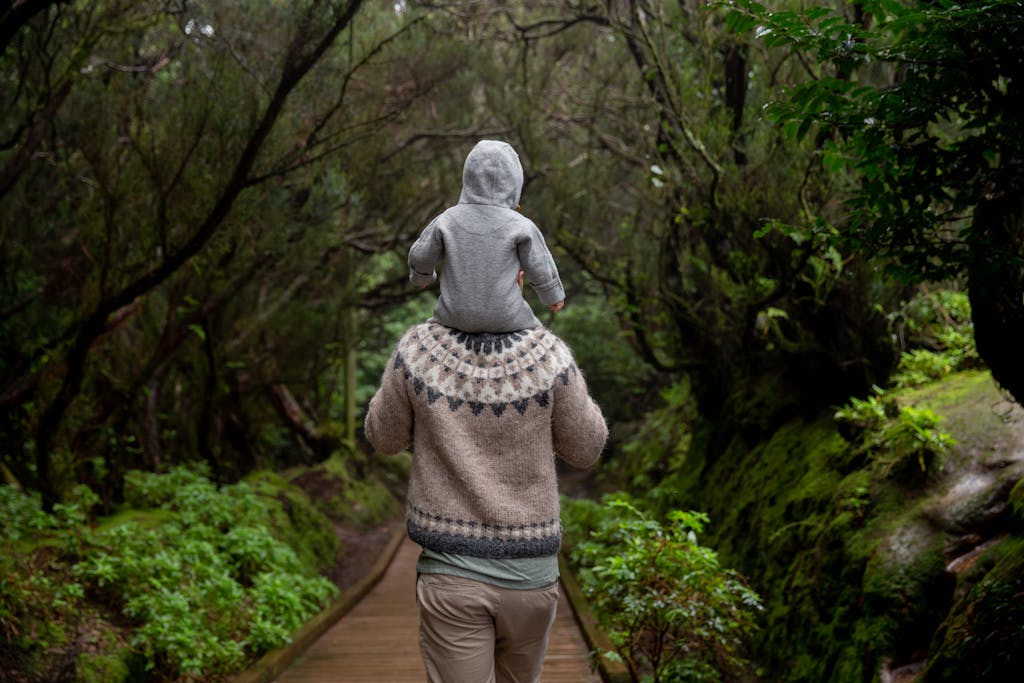 A father carrying his child on a forest path, enjoying nature and bonding on an autumn day.