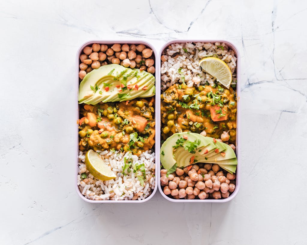 Delicious vegan lunchboxes featuring chickpeas, rice, avocado, and curry on a white background.